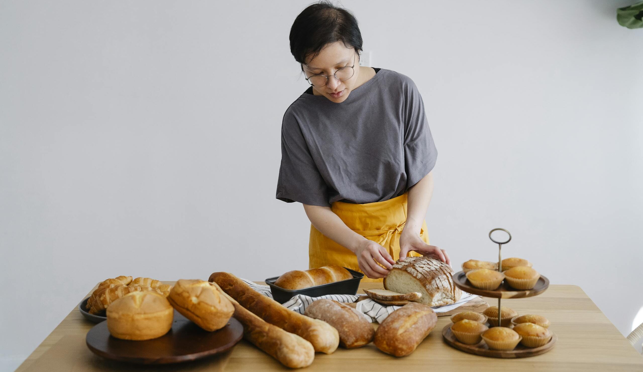 A woman wearing an apron slices freshly baked bread on a wooden table.